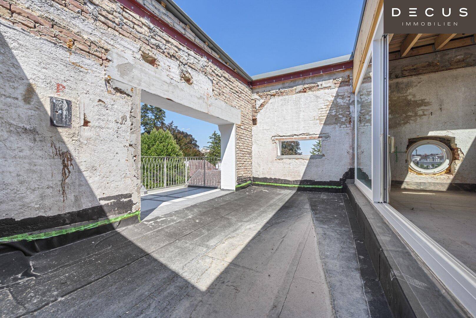 Dachterrasse im Rohbau mit Blick auf die Umgebung und den Innenraum durch Fenster.