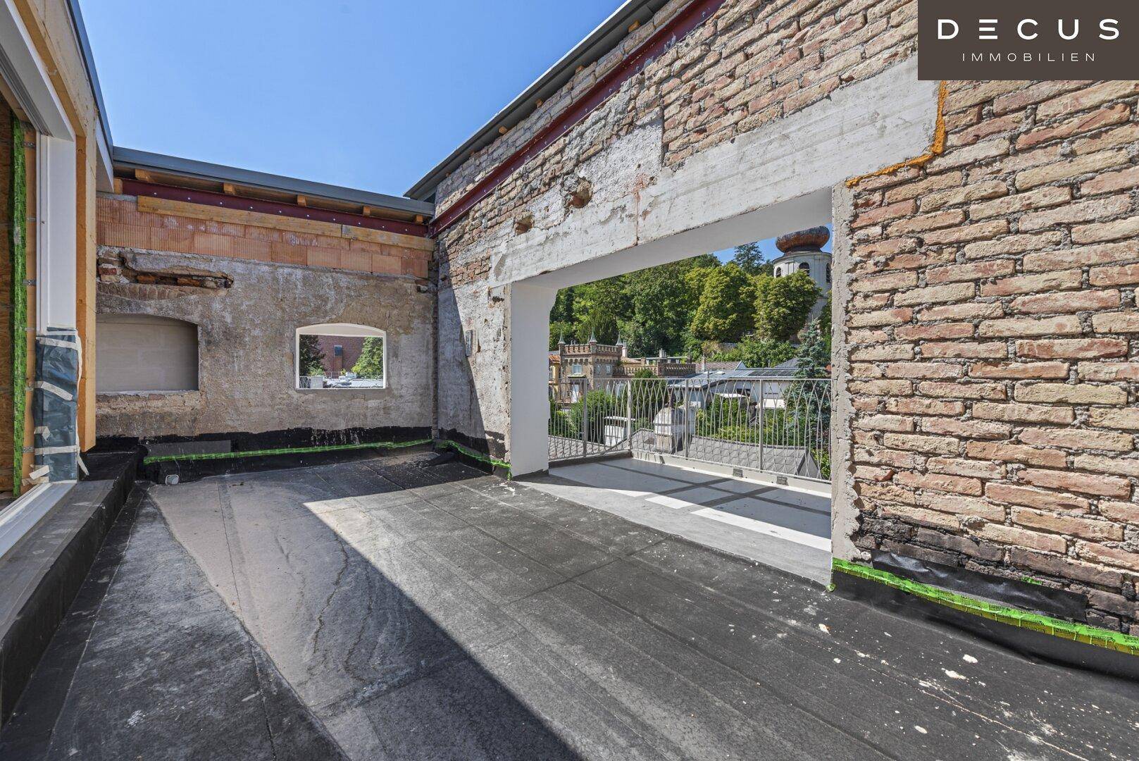 Dachterrasse im Rohbau mit Ziegelwänden und Blick auf die Stadt.