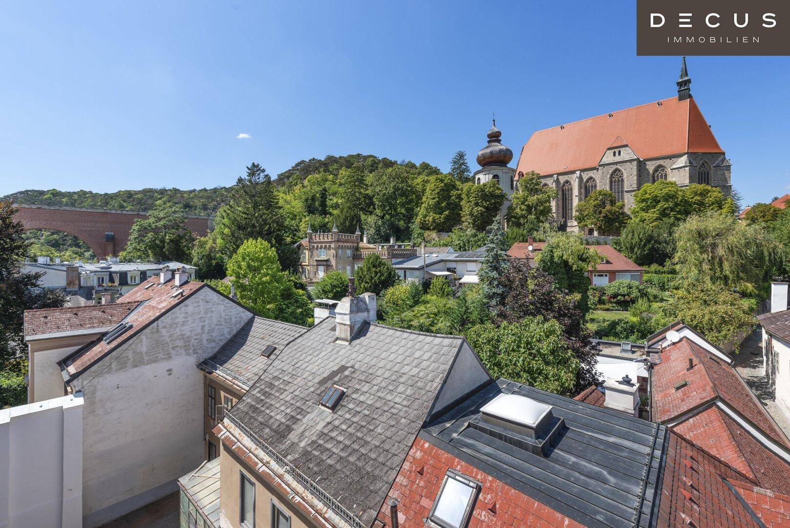 Panoramablick über die Dächer der Stadt mit historischer Kirche und grüner Umgebung.