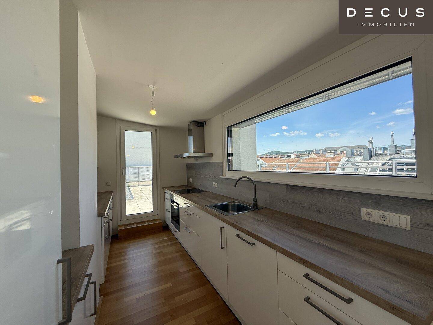 Helle Küche mit großem Fenster, Spülbecken und Blick auf die Stadt, ausgestattet mit modernen Geräten.