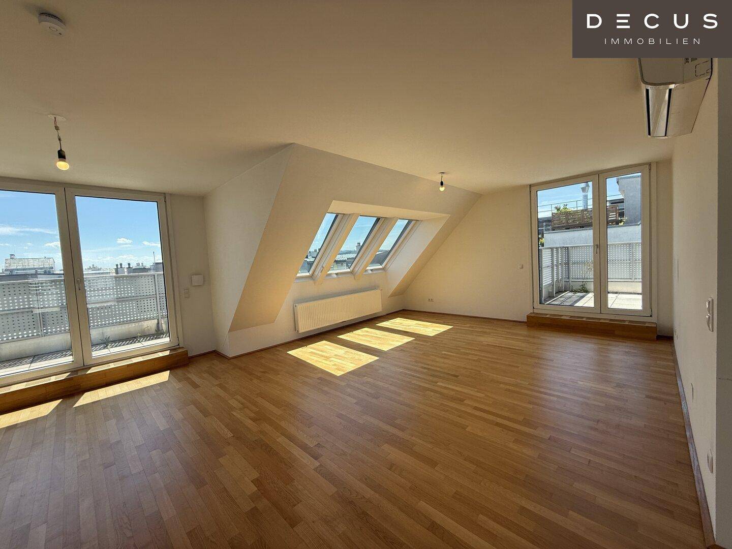 Heller Wohnbereich mit Parkettboden, Dachschrägen und großen Fenstern mit Zugang zur Terrasse.
