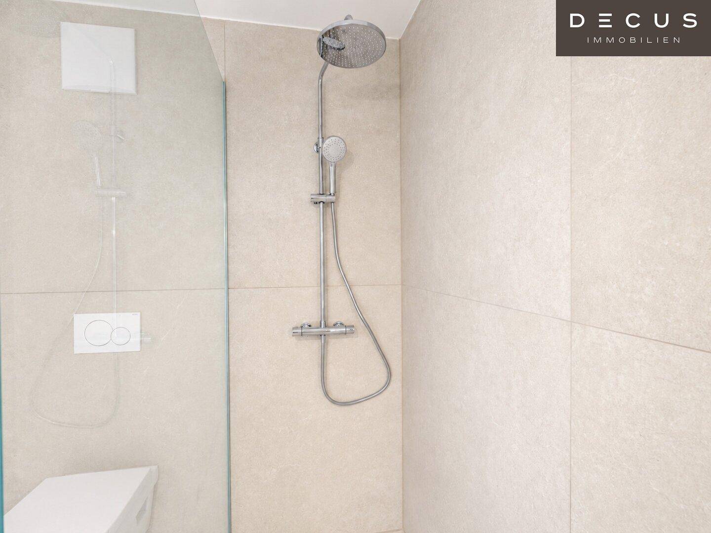 Detailansicht der modernen ebenerdigen Dusche mit Regenduschkopf und hellen Fliesen.