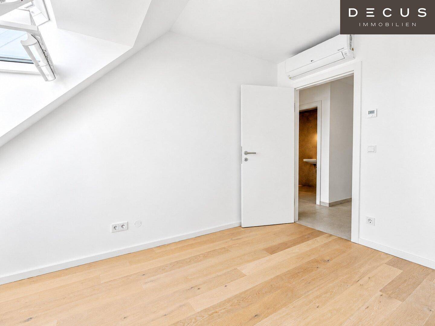 Helles Zimmer mit Holzboden, Klimaanlage und Zugang zu einem modernen Badezimmer.