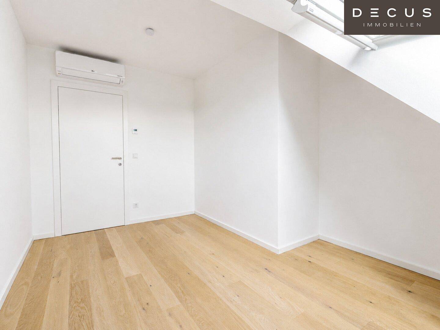 Helles Zimmer mit Holzboden, weißer Tür und Klimaanlage, bereit zur individuellen Gestaltung.