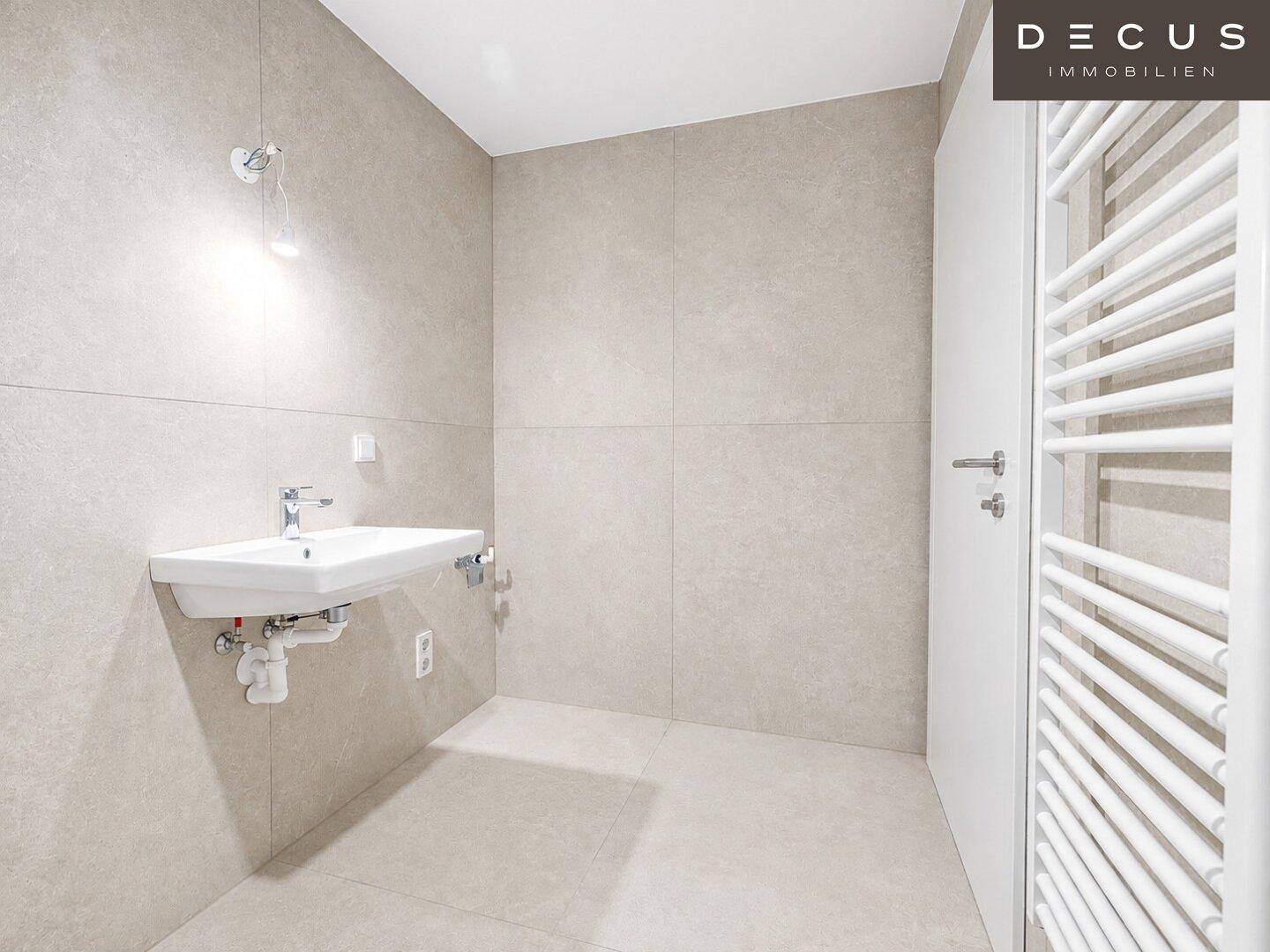 Modernes Badezimmer mit Waschbecken und beheiztem Handtuchhalter in hellen, neutralen Fliesen.