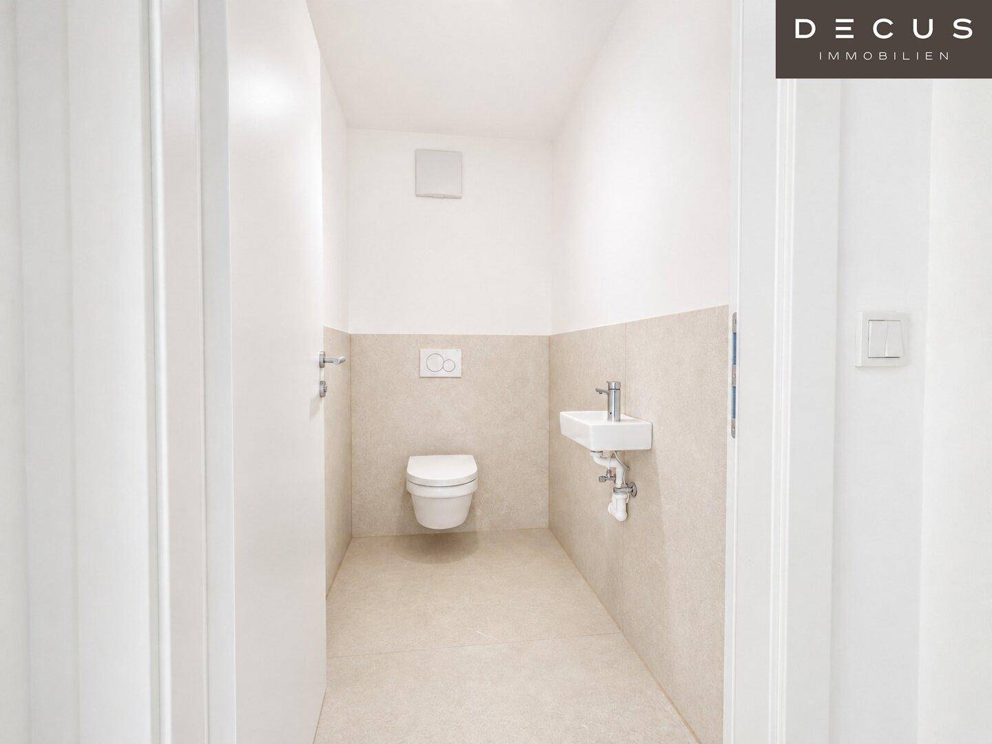 Modernes Gäste-WC mit wandhängender Toilette und kleinem Waschbecken in hellen Fliesen.