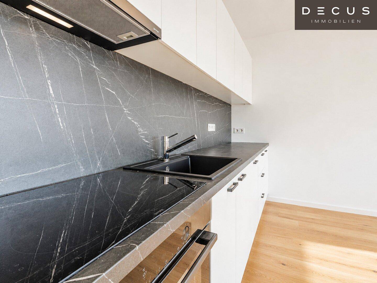 Detailansicht der modernen Küche mit dunkler Arbeitsplatte, Spüle und integriertem Backofen.