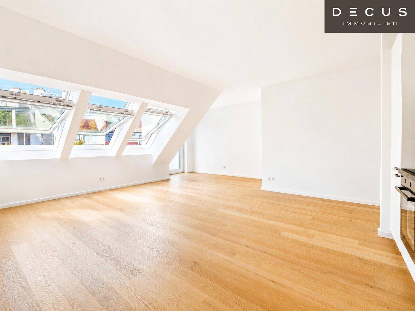 Geräumiger, heller Raum mit Holzboden, Dachfenstern und Zugang zu einem Balkon oder einer Terrasse.