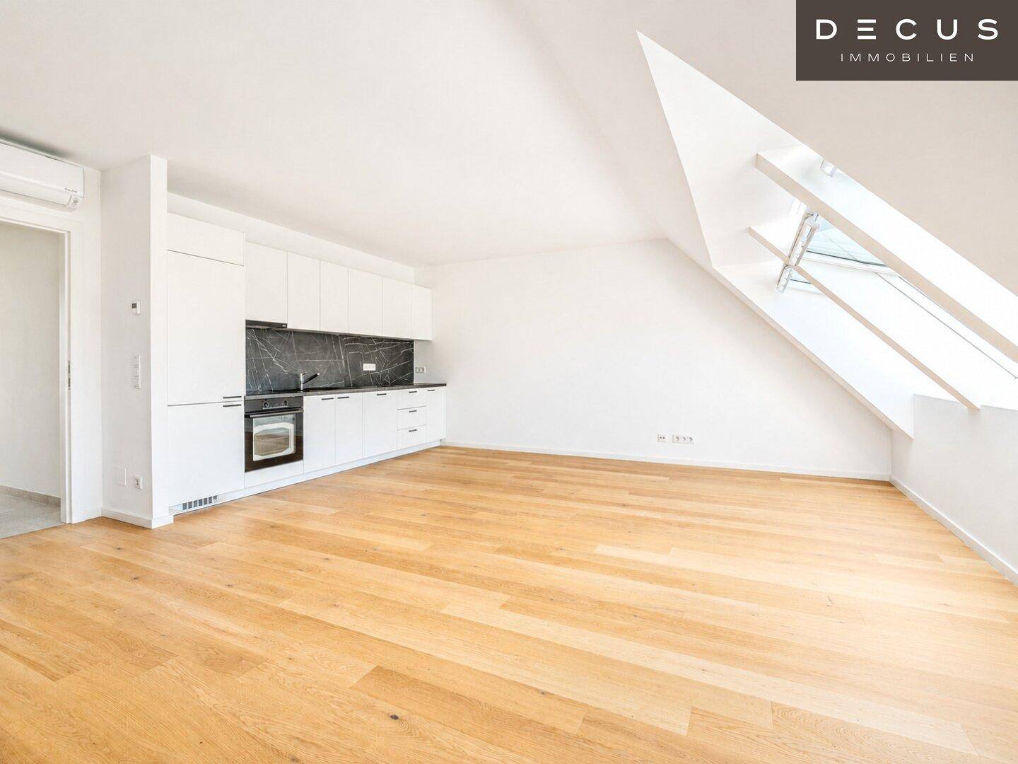 Offene Küche mit weißen Schränken, dunkler Arbeitsplatte und Dachfenster in einem hellen Raum.