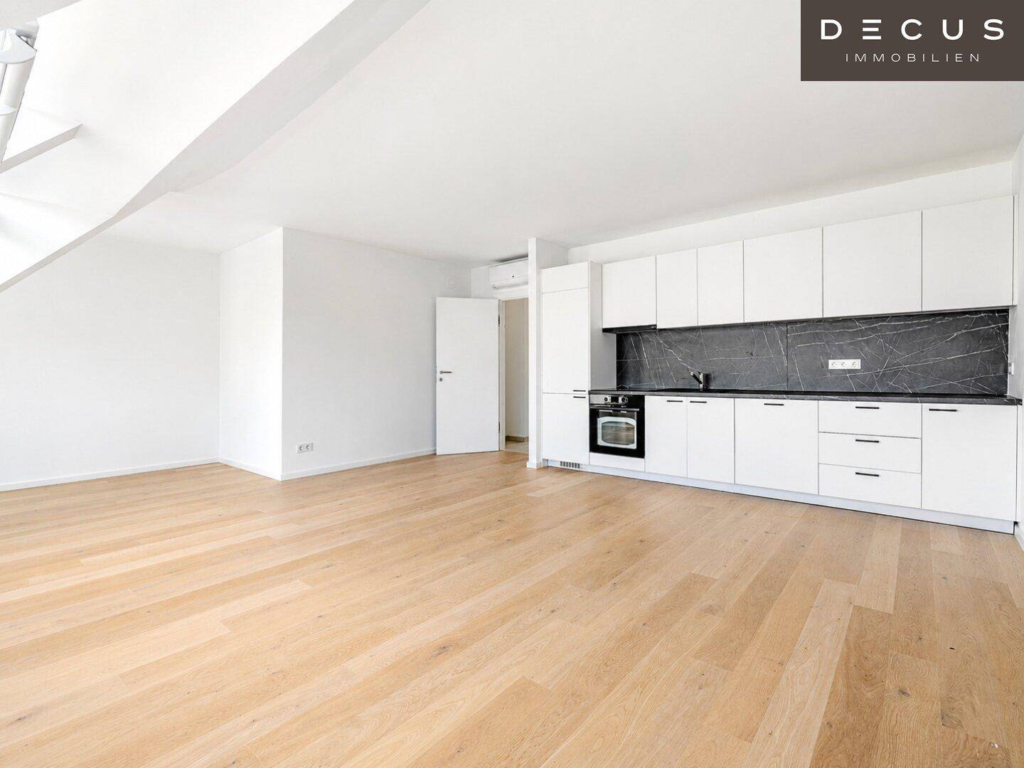 Moderne Einbauküche mit weißen Schränken, dunkler Arbeitsplatte und offenem Wohnbereich.