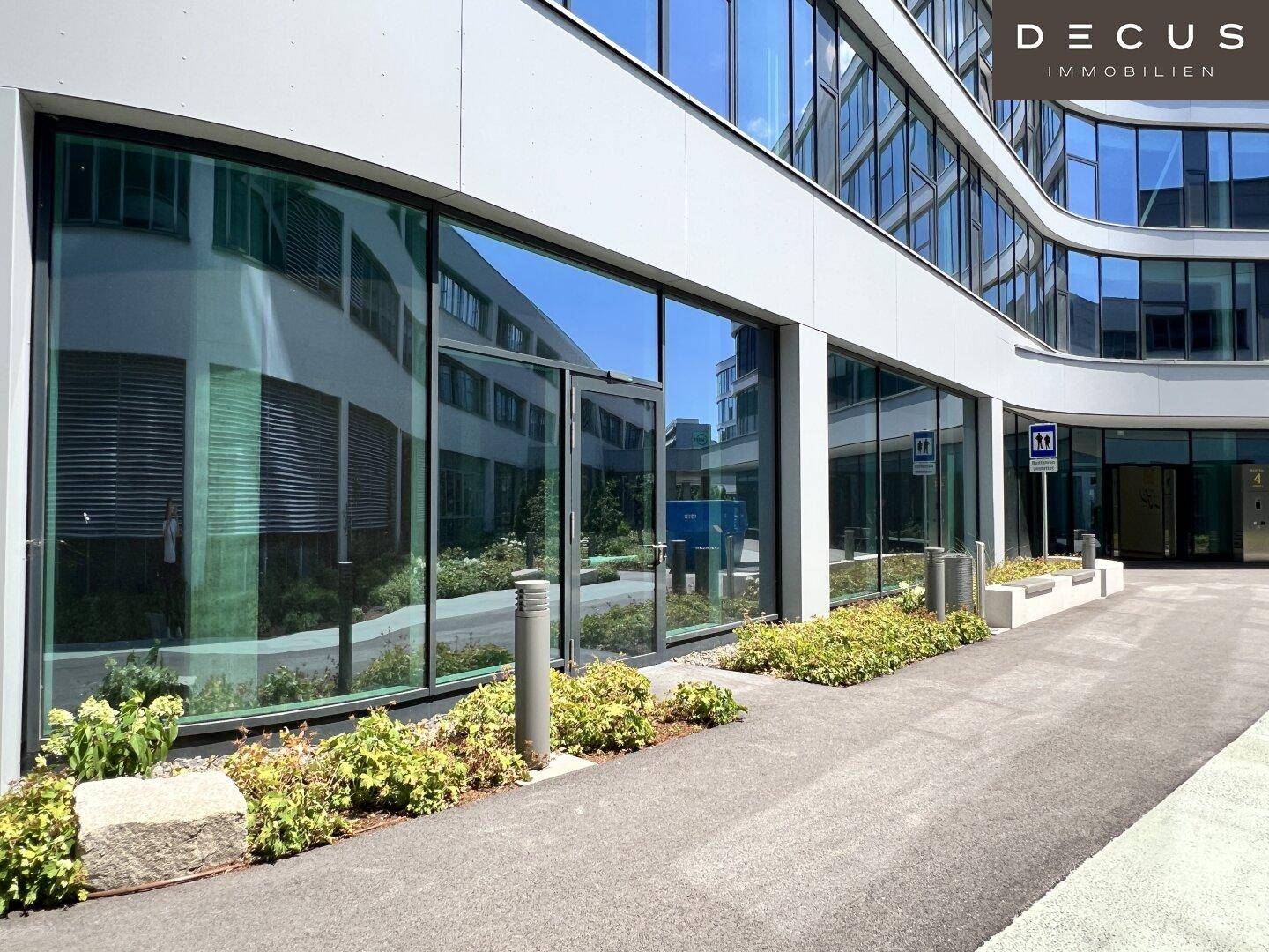 Eingangsbereich eines modernen Geschäftsgebäudes mit großen Glasfronten und Außenbeleuchtung.
