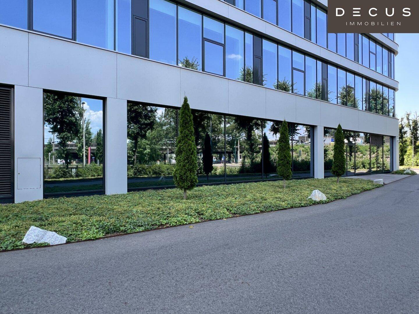 Erdgeschoss eines modernen Bürogebäudes mit großen Fensterfronten und gepflegter Grünanlage.