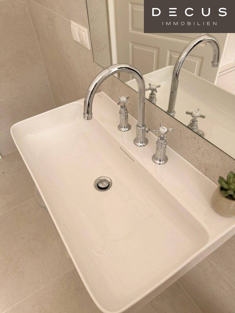 Modernes Waschbecken mit zwei Armaturen und Spiegel in einem hellen Badezimmer.