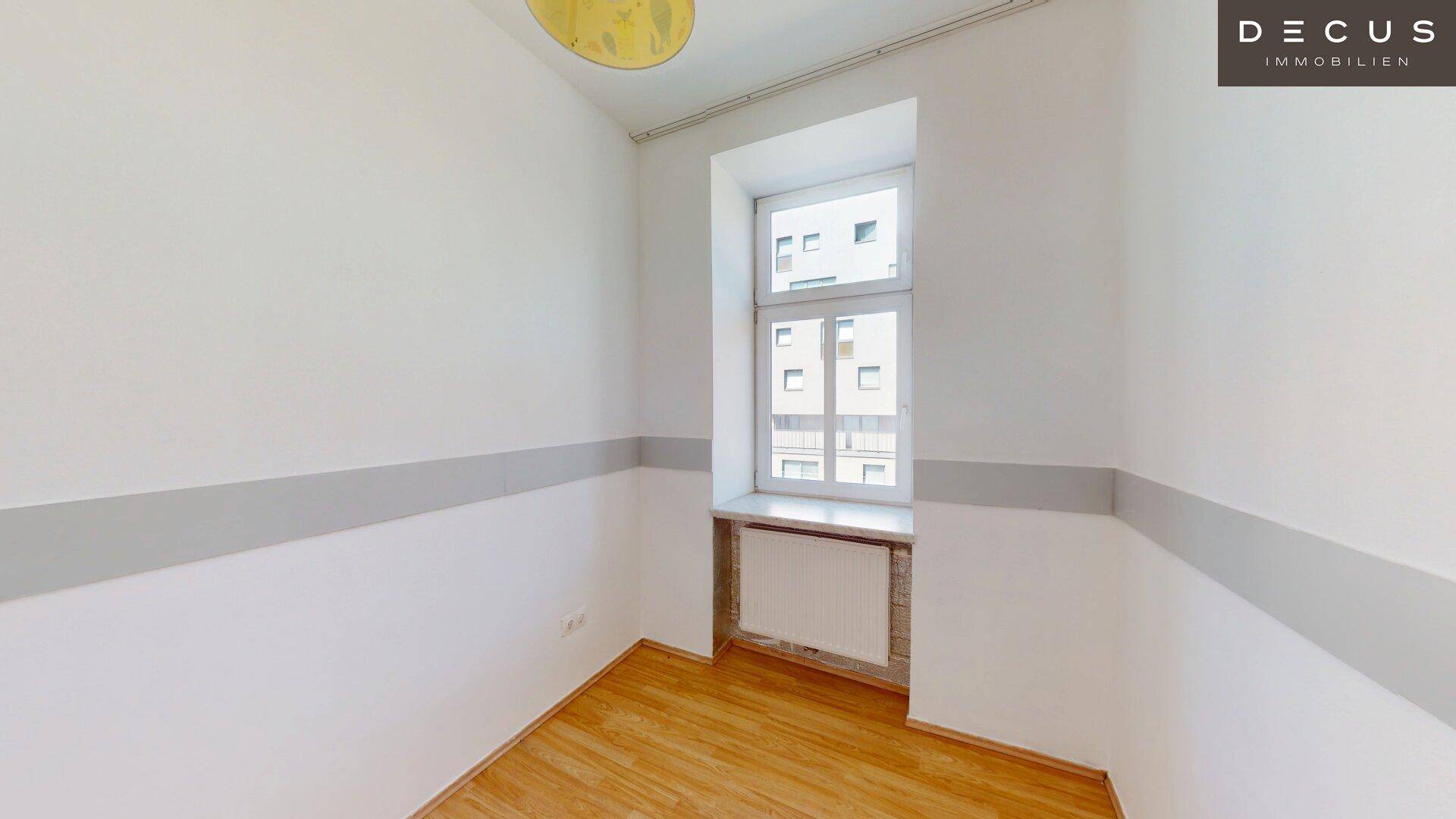 Kleineres Zimmer mit Holzfußboden und einem Fenster, das Tageslicht hereinlässt.