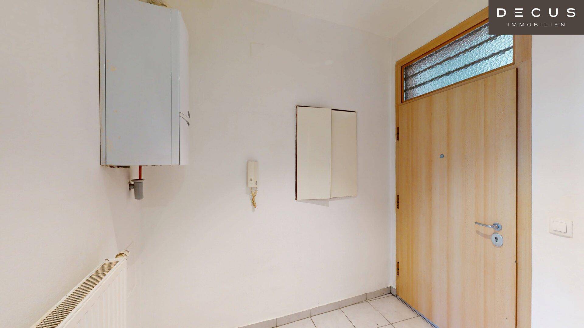 Eingangsbereich mit Holztür, Fliesenboden und einem Heizkessel an der Wand.
