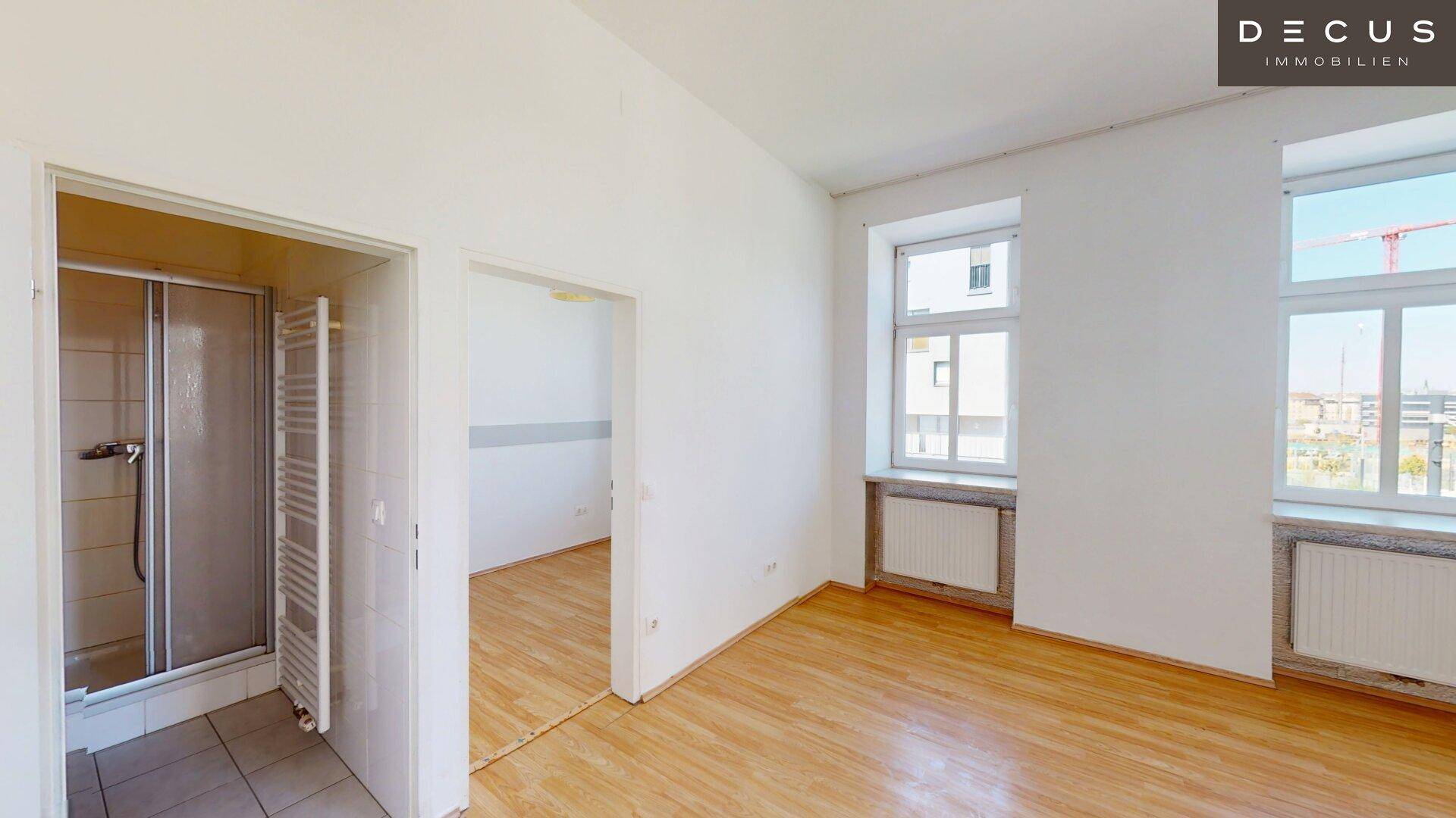 Helles Zimmer mit Holzfußboden und Zugang zu einem Badezimmer mit Duschkabine.