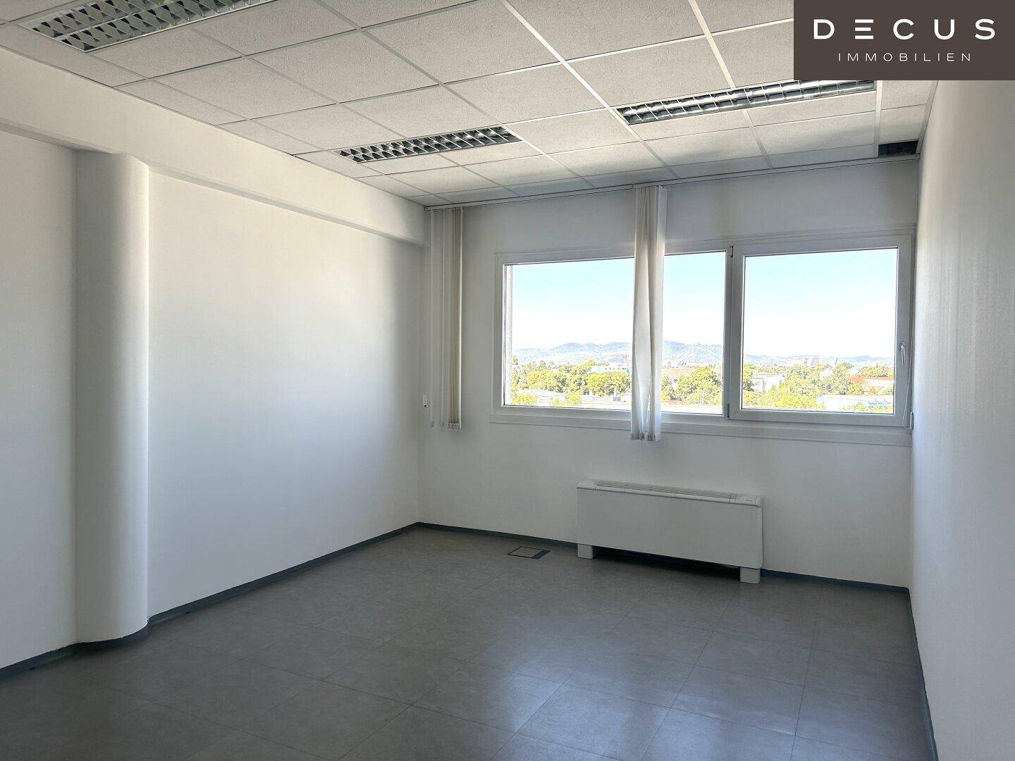 Heller Büroraum mit weitem Ausblick, großen Fenstern und grauem Fliesenboden, ideal für produktives Arbeiten.