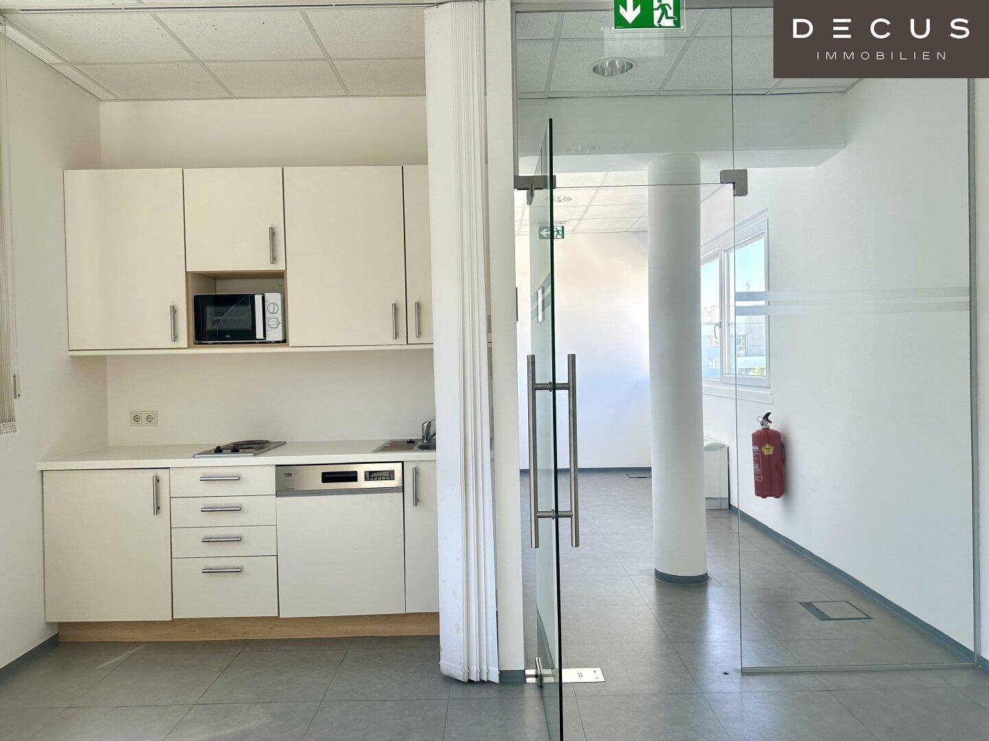 Kleine Küchenzeile in einem Bürobereich mit Mikrowelle, Spülmaschine und praktischer Glaswandabtrennung.