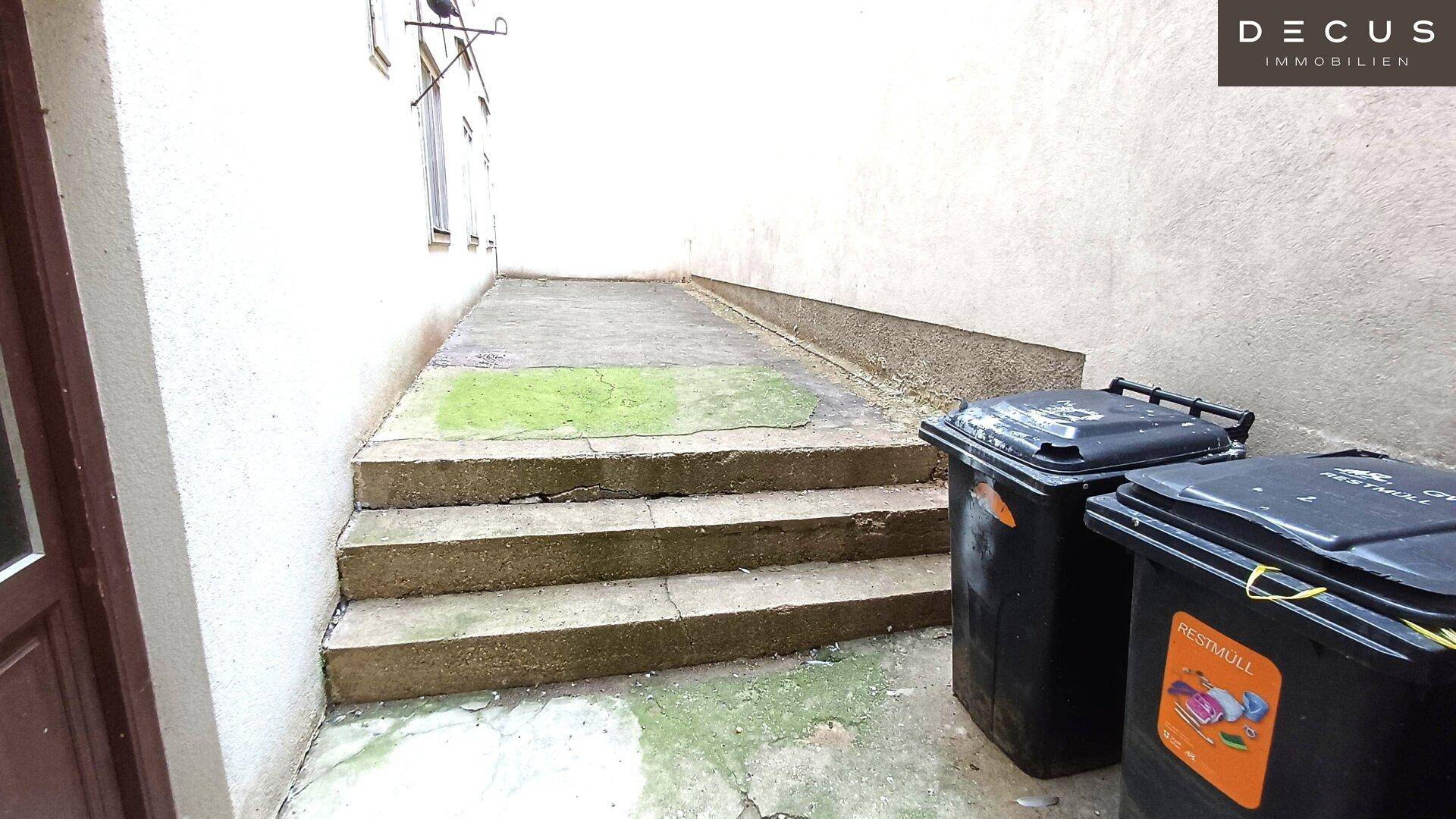 Außentreppe oder Rampe mit zwei Mülltonnen, die zu einem oberen Bereich führt.