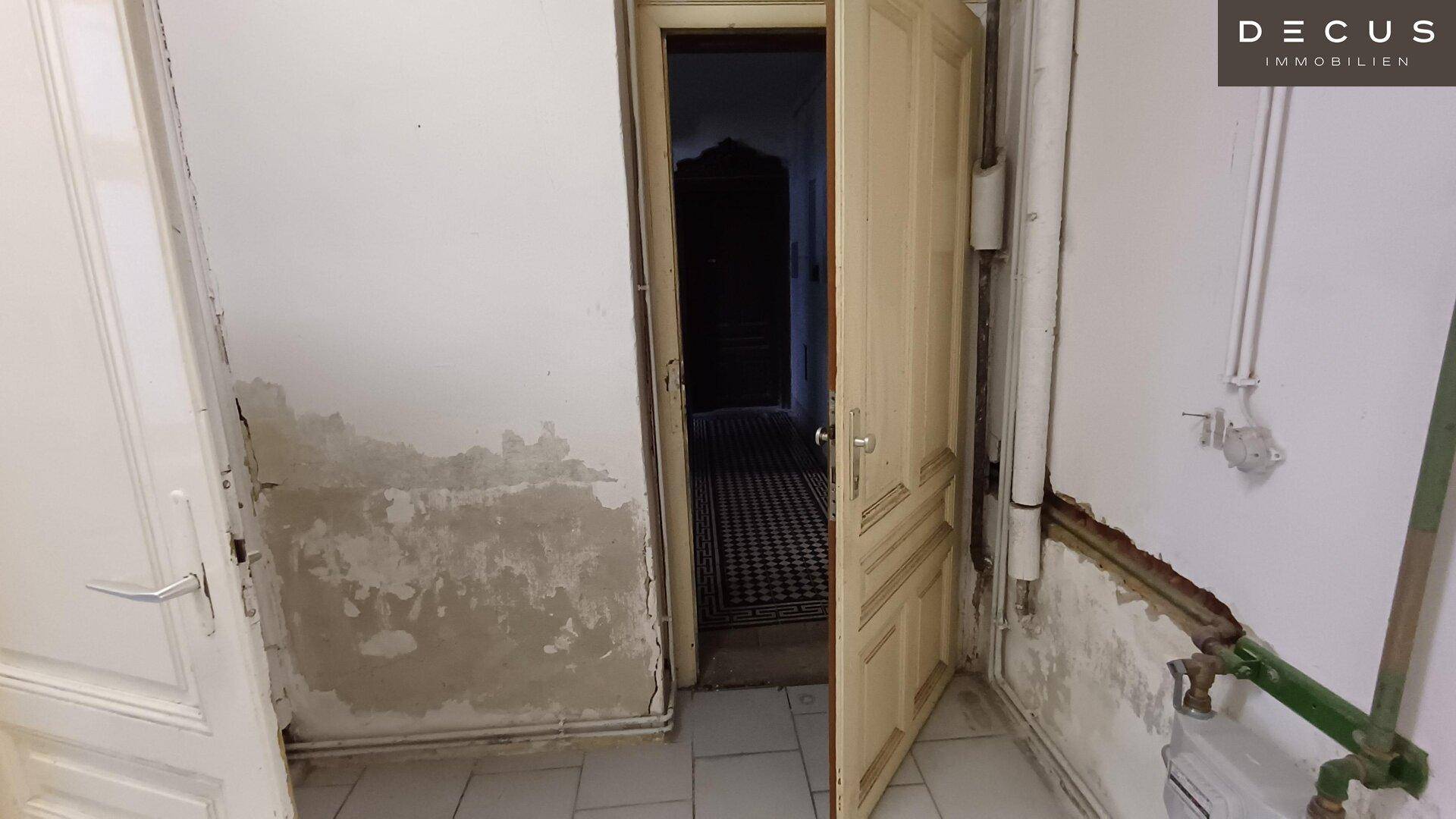 Flur oder Eingangsbereich mit Fliesenboden, freigelegten Wänden und offenen Türen.