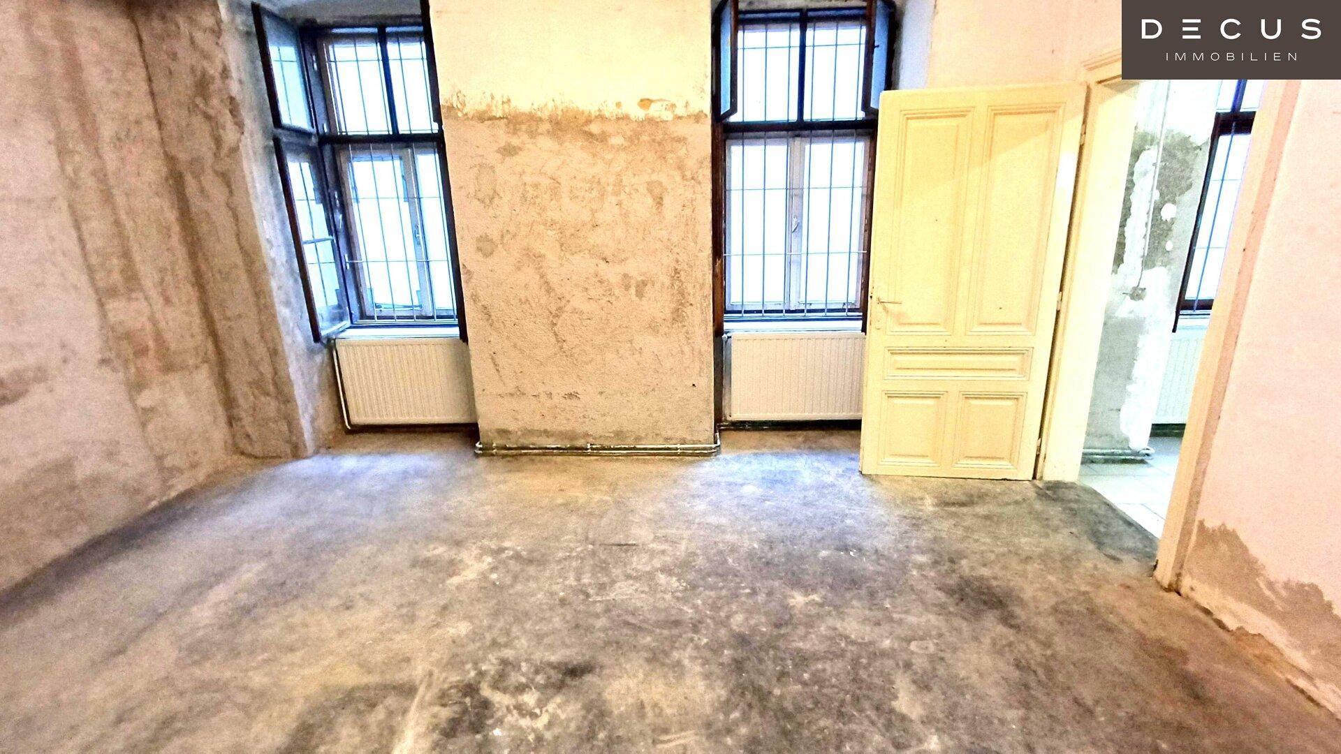 Sanierungsbedürftiger Raum mit freigelegten Wänden, zwei alten Fenstern und Heizkörpern darunter.