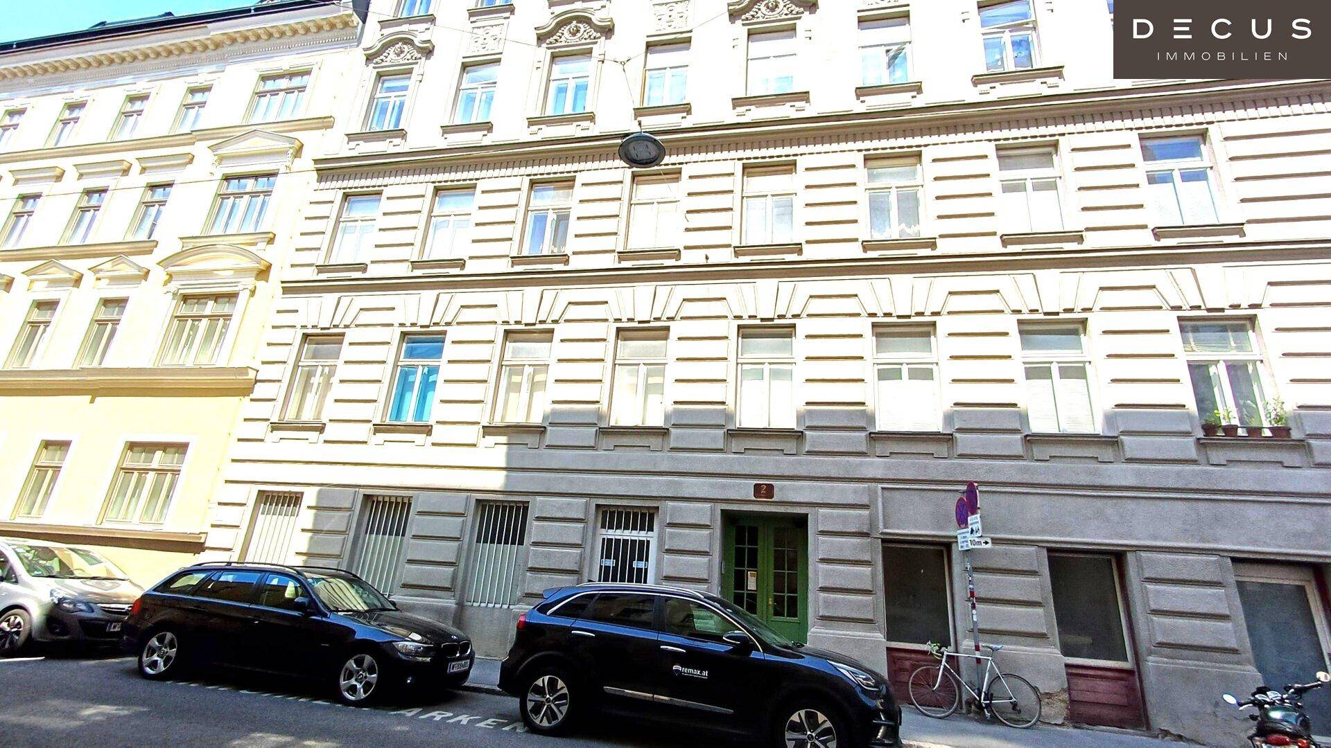 Fassade eines Mehrfamilienhauses an einer Straße mit geparkten Autos und vielen Fenstern.