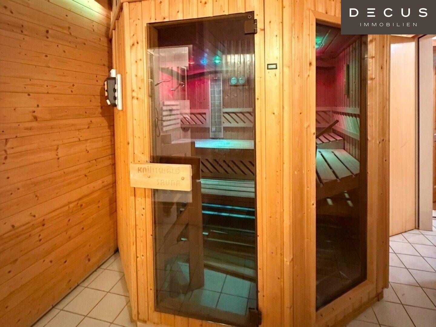 Moderne Saunakabine mit Glastür und farbiger Beleuchtung in einem Holzambiente.