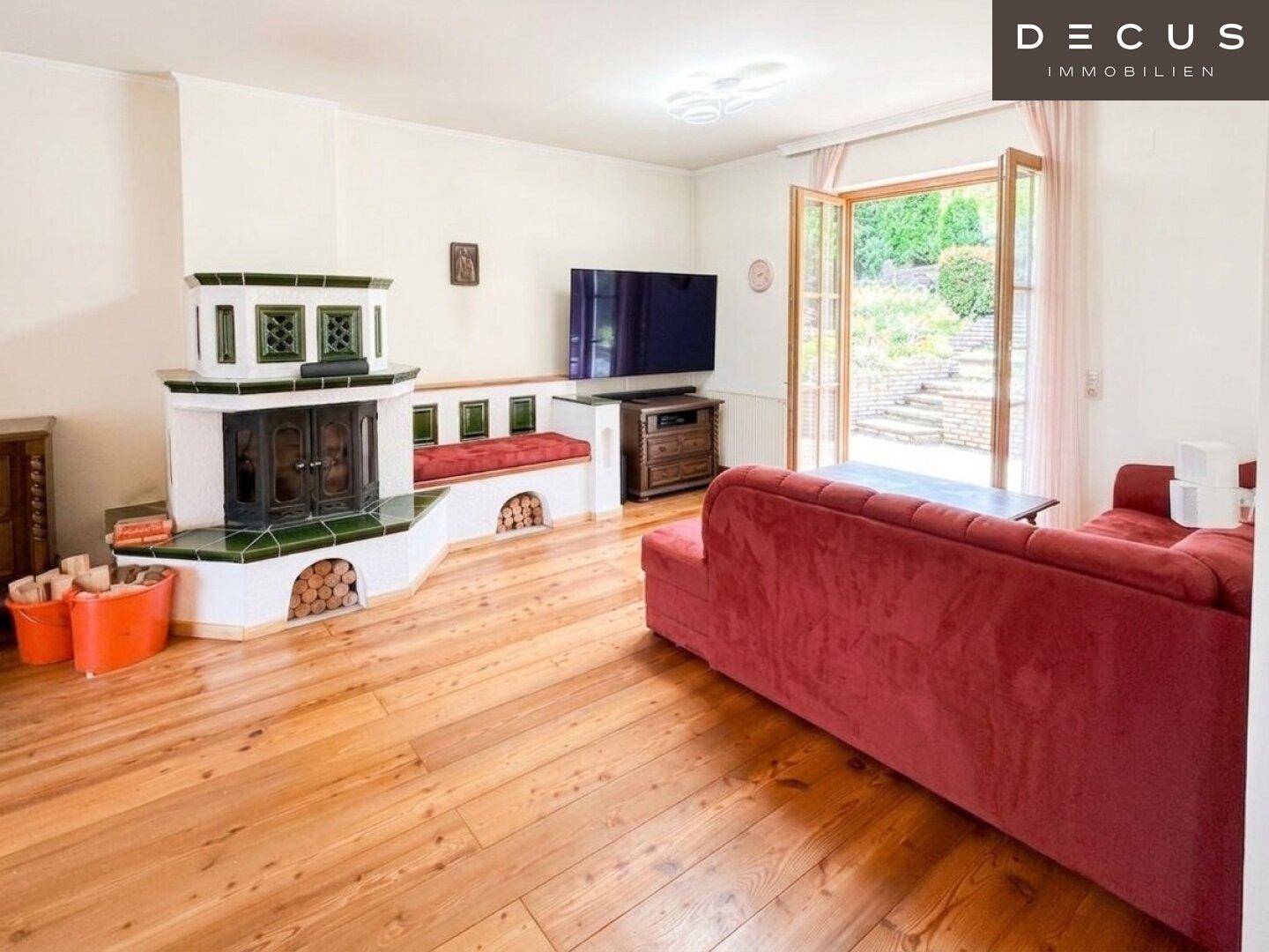 Helles Wohnzimmer mit traditionellem Kachelofen, Holzboden und direktem Zugang zum Garten.