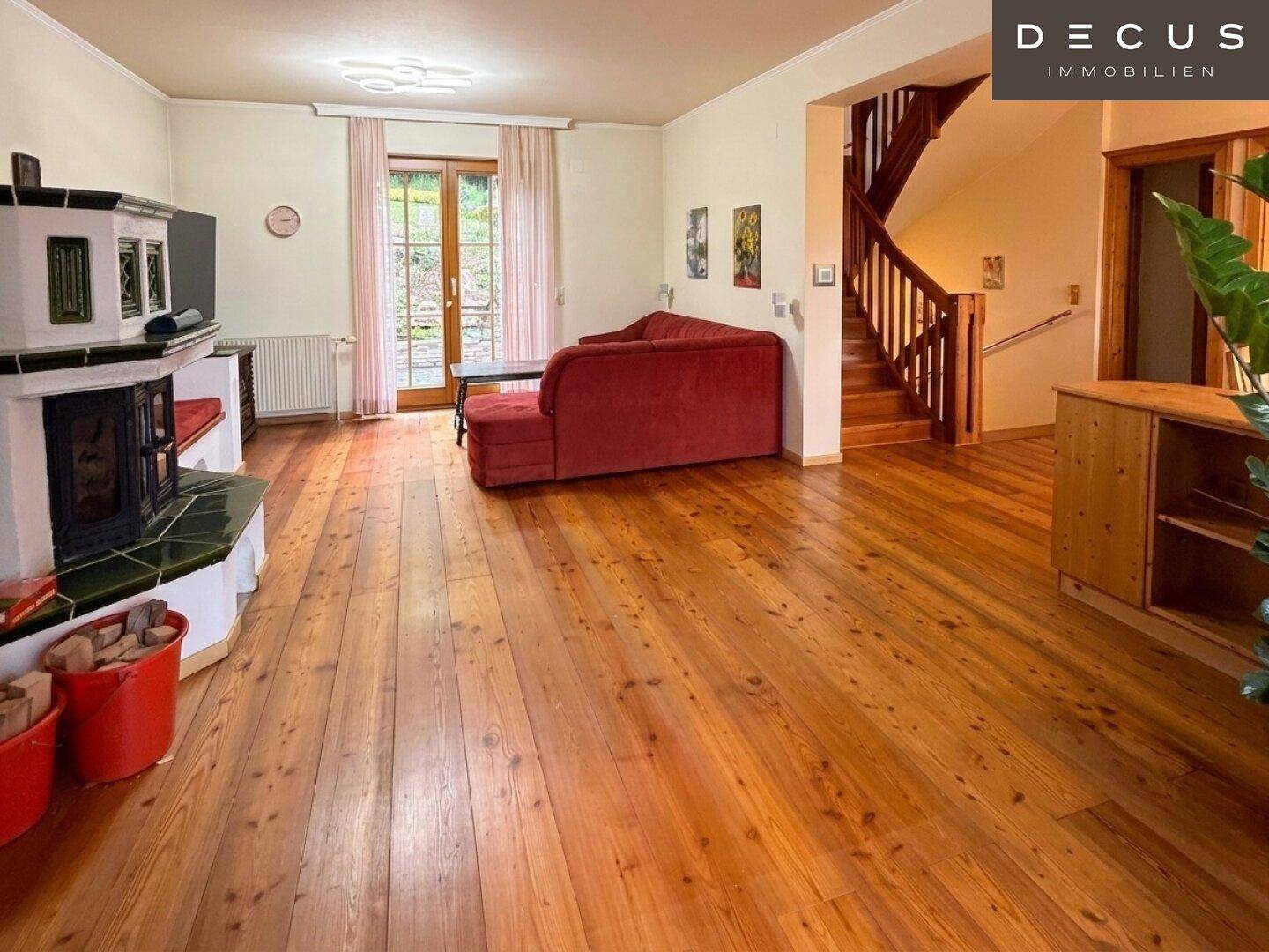 Gemütliches Wohnzimmer mit Kachelofen, Holzfußboden und Treppe zum Obergeschoss.