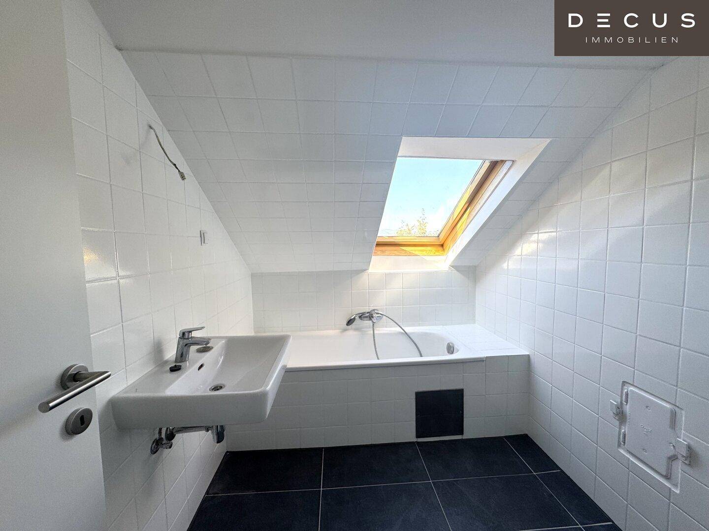 Modernes Badezimmer mit Badewanne unter einem Dachfenster und weißen Wandfliesen.