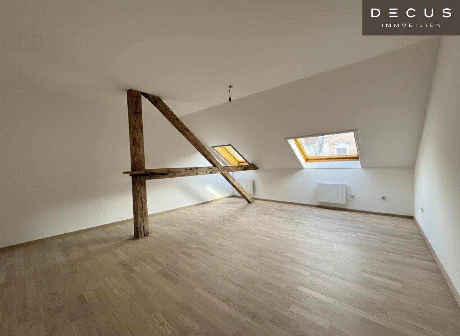 Geräumiger Dachraum mit sichtbaren Holzbalken, Laminatboden und zwei Dachfenstern.