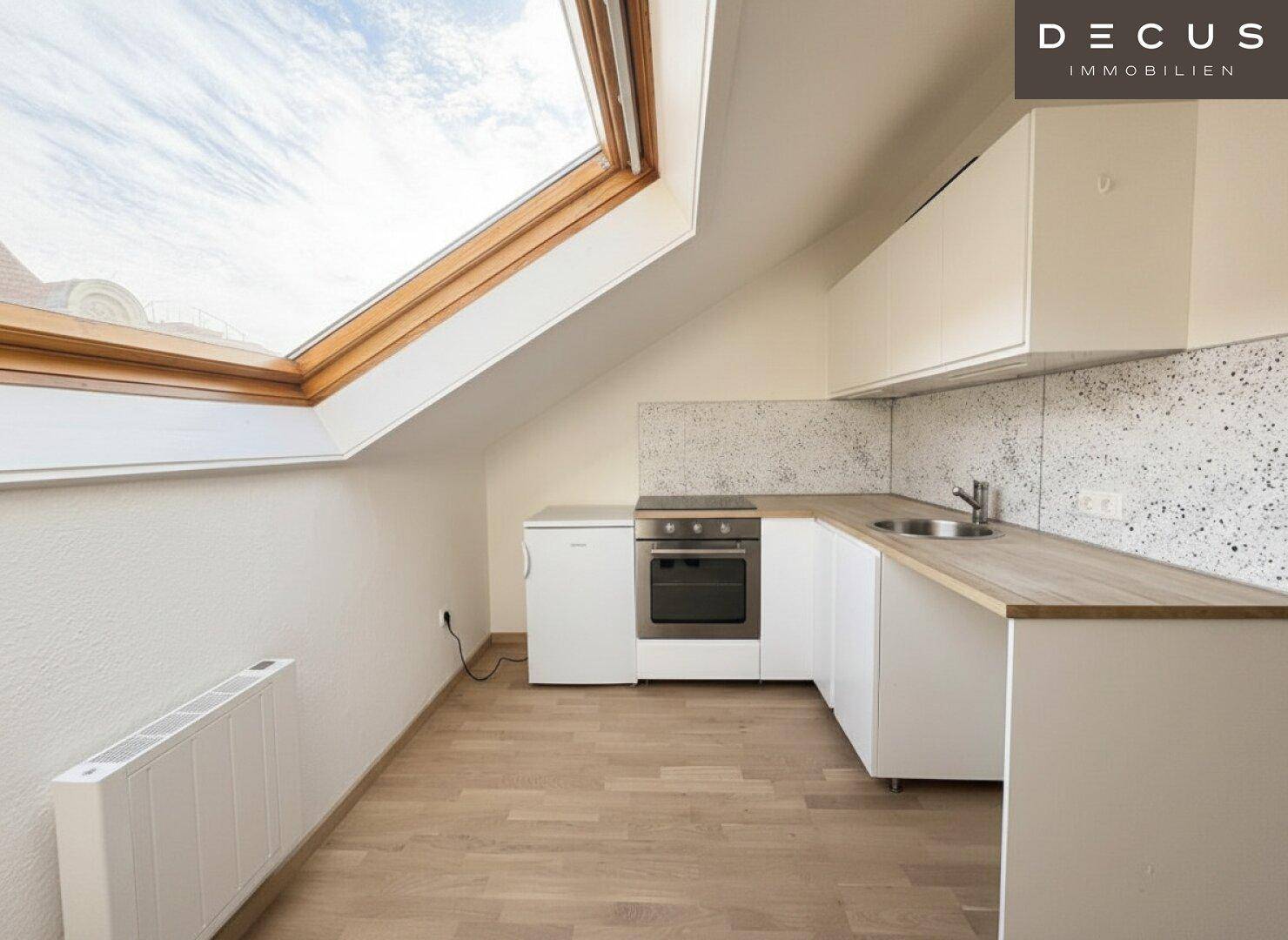 Funktionale Küchenzeile mit hellen Holz-Arbeitsplatten und integriertem Backofen unter einem Dachfenster.