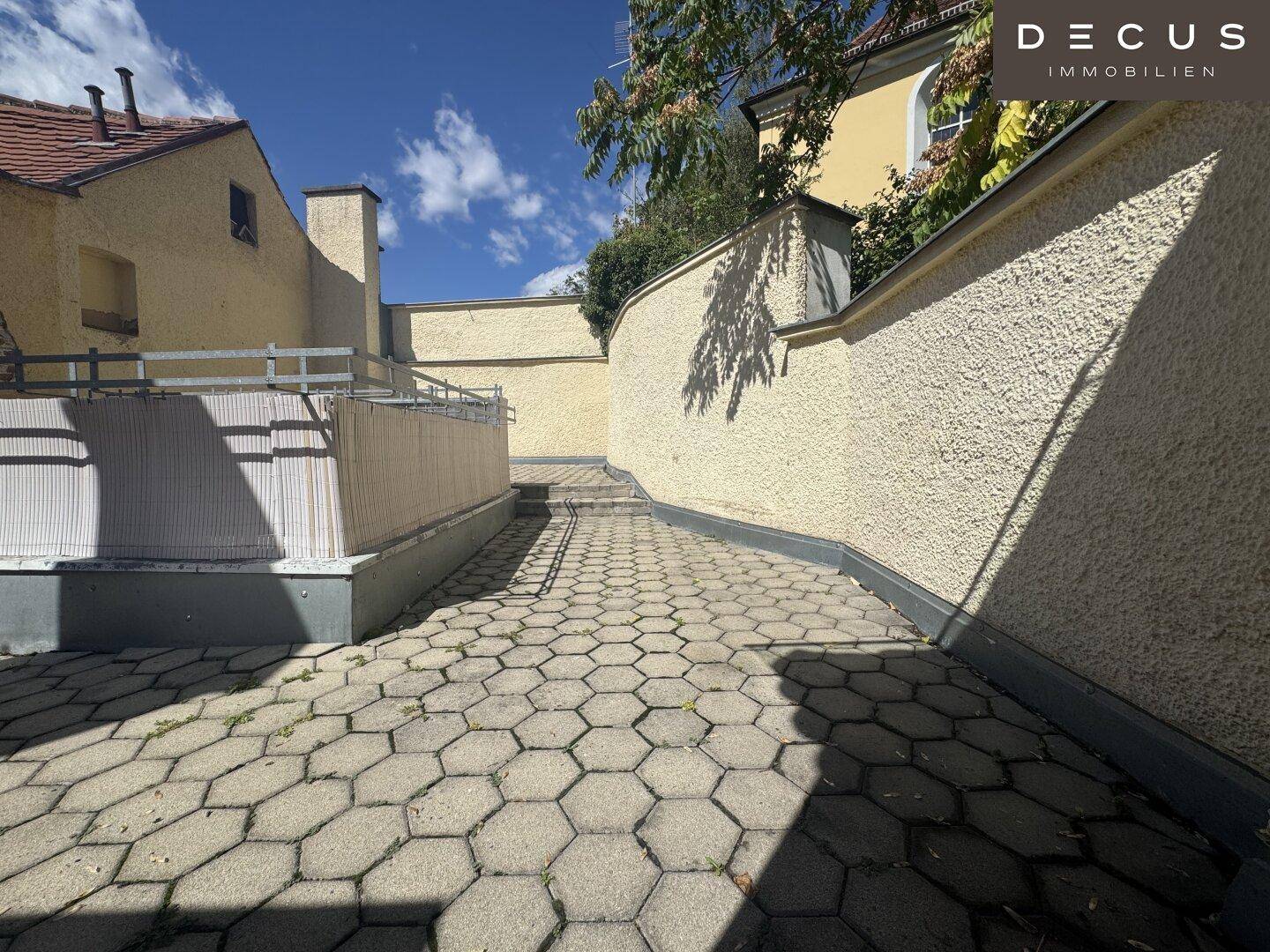 Gepflasterte Terrasse mit hohen Mauern und Treppen, bietet einen privaten Außenbereich.