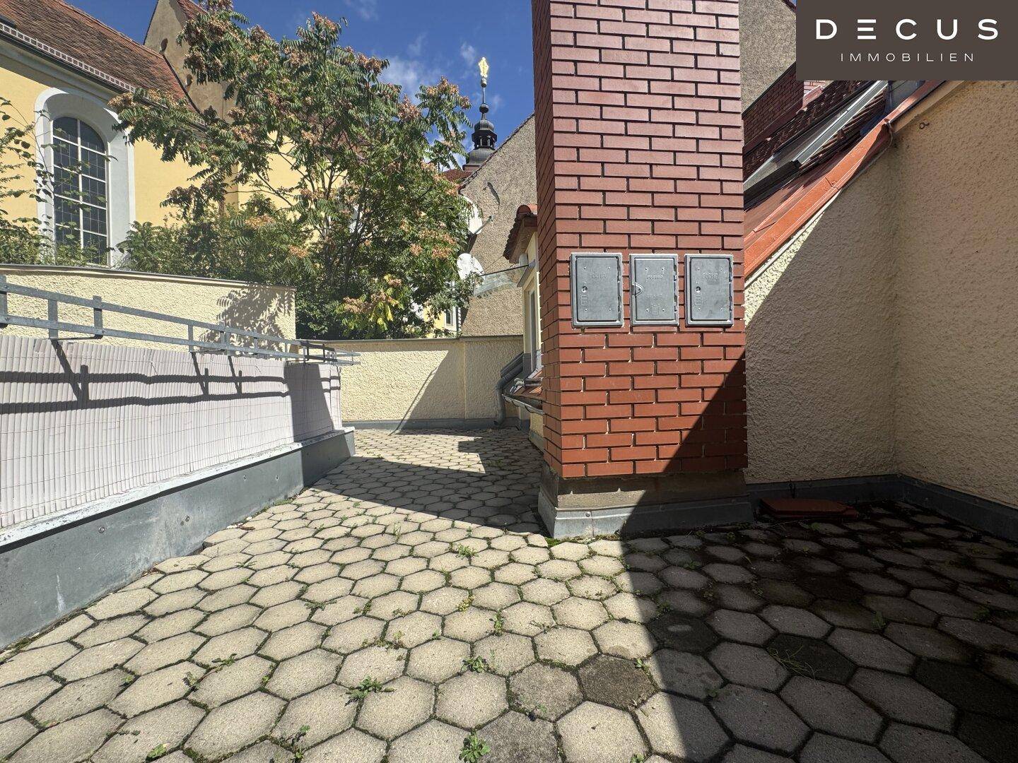 Gepflasterte Terrasse mit Ziegelkamin und hohen Mauern, bietet einen geschützten Außenbereich.