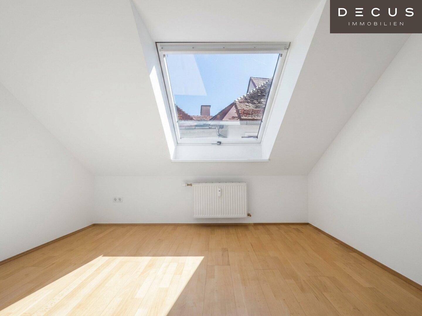 Leeres Wohnzimmer im Dachgeschoss mit Holzboden und großem Dachfenster, bietet viel Tageslicht.