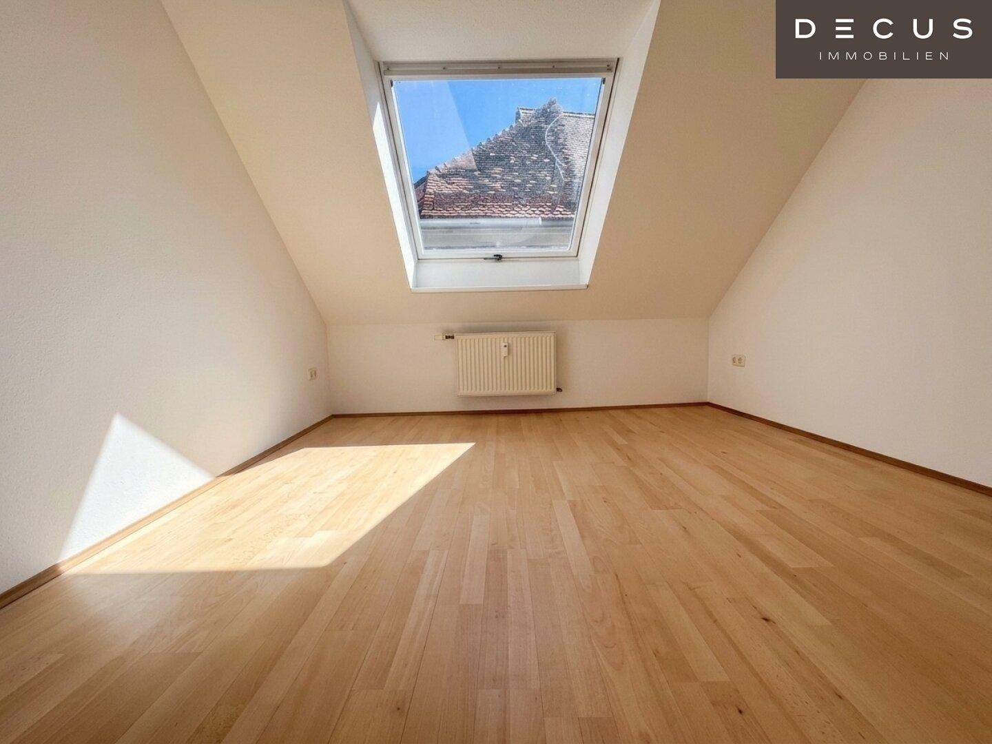 Leeres Schlafzimmer im Dachgeschoss mit Holzboden und großem Dachfenster, bietet viel Licht.
