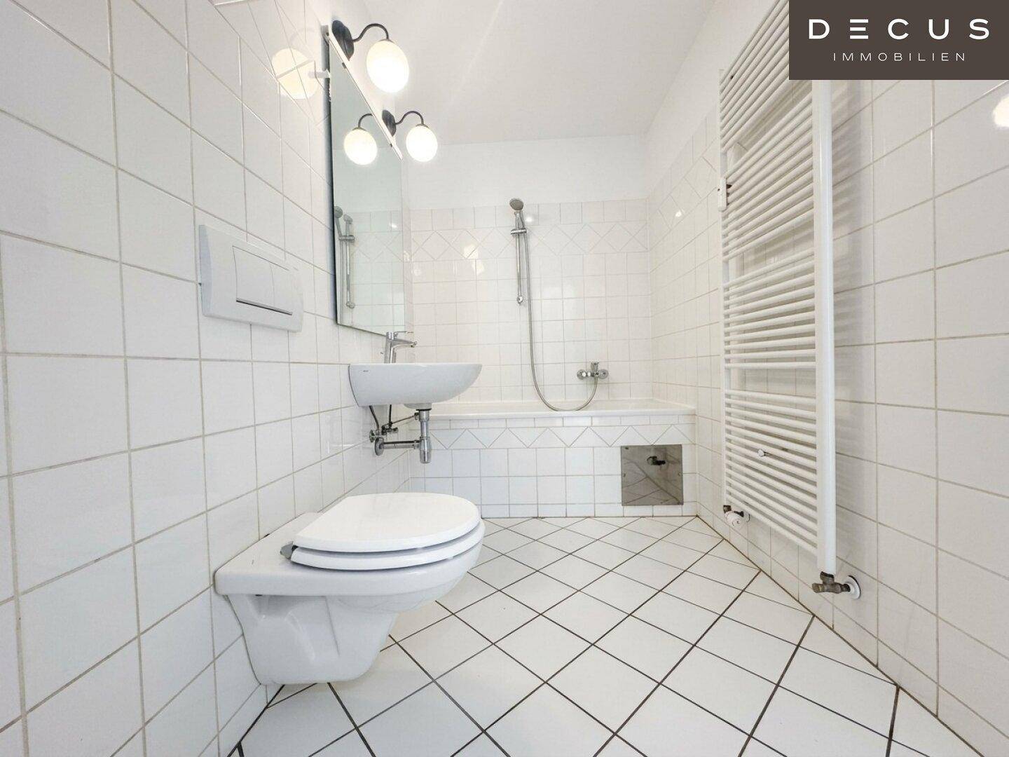 Gefliestes Badezimmer in Weiß mit Badewanne, Toilette und Waschbecken, inklusive Handtuchheizkörper.