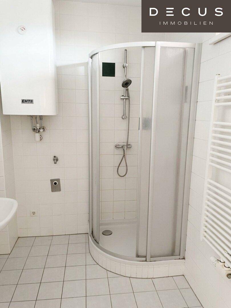 Badezimmer mit weiß gefliesten Wänden, einer Duschkabine und einem praktischen Handtuchheizkörper.