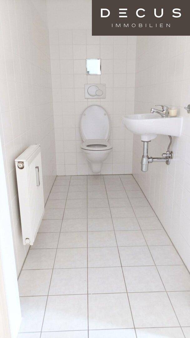 Separates WC mit weiß gefliesten Wänden, Toilette und Waschbecken, in gutem Zustand.