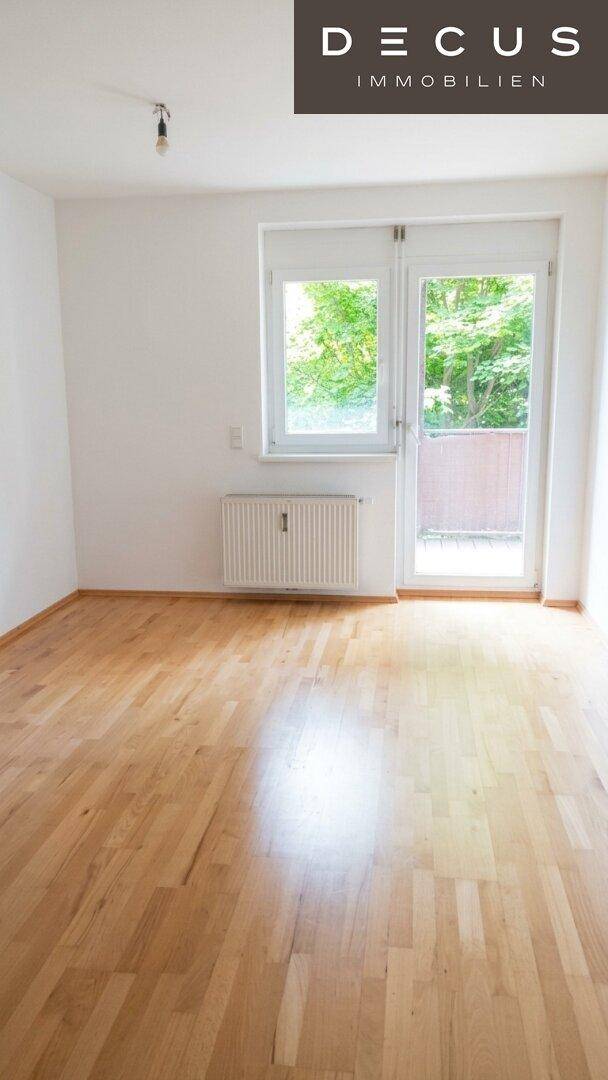 Heller Raum mit Parkettboden, großem Fenster und Zugang zu einem Außenbereich, ideal als Wohnzimmer.