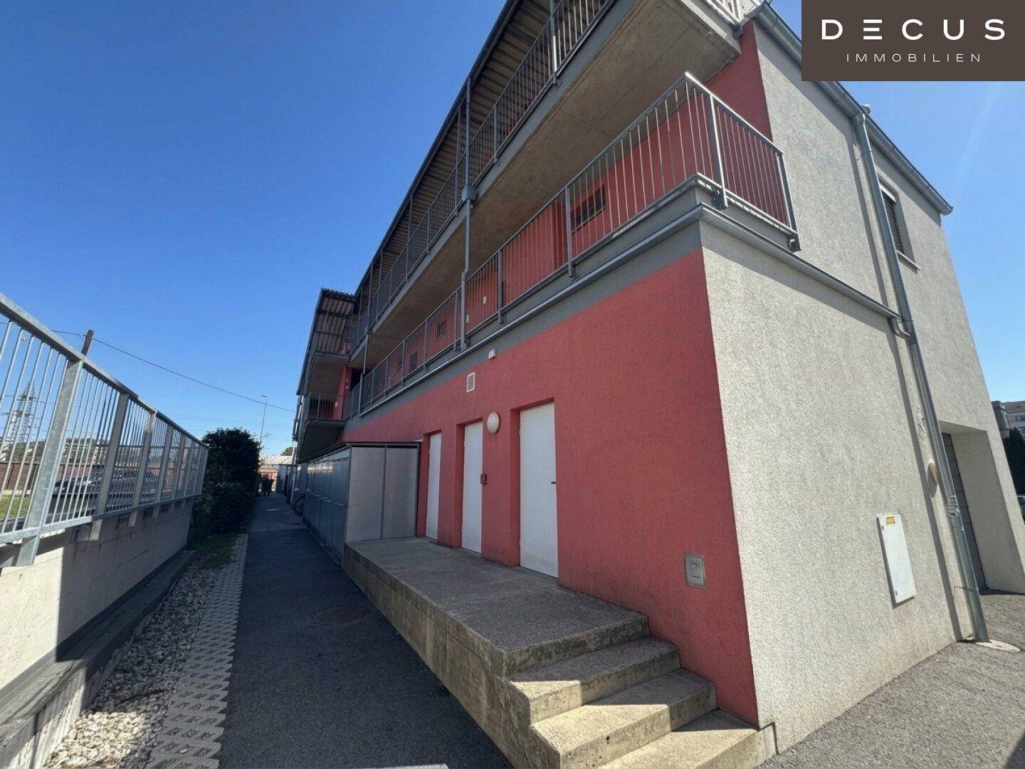 Seitlicher Zugangsbereich des Gebäudes mit mehreren Türen und einer Treppe, umgeben von einem Gehweg.