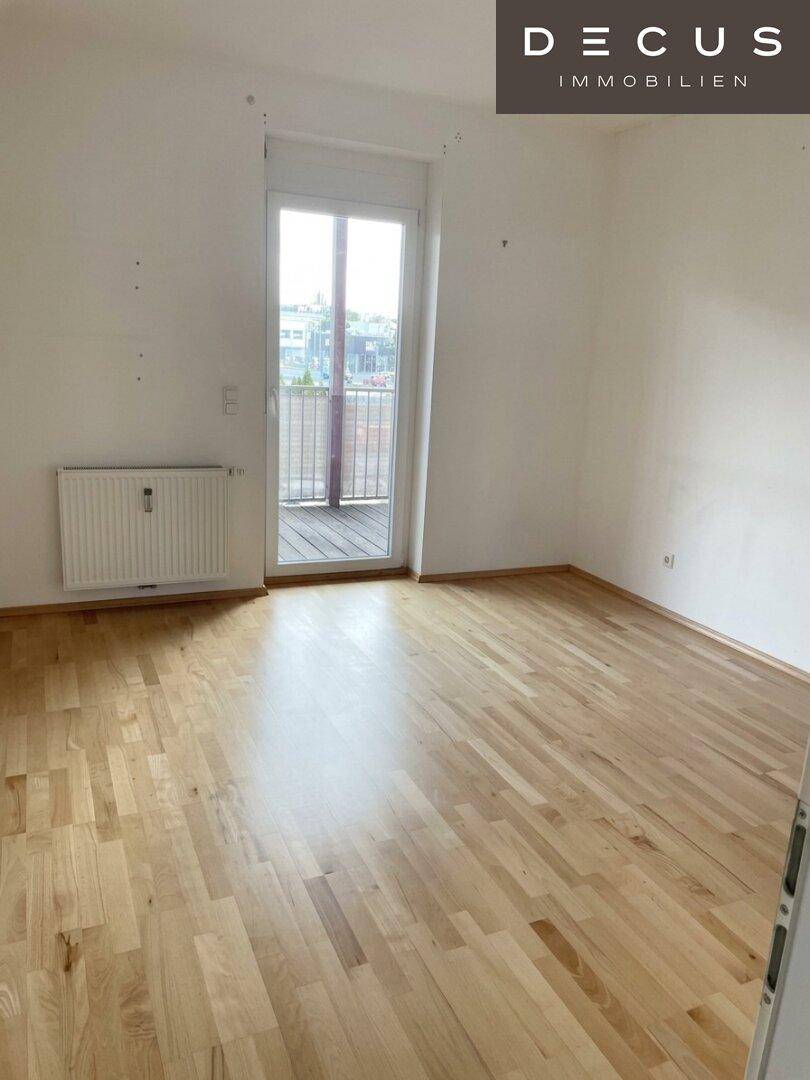 Geräumiges Zimmer mit hellem Parkettboden und direktem Zugang zu einem Balkon, gut belichtet.