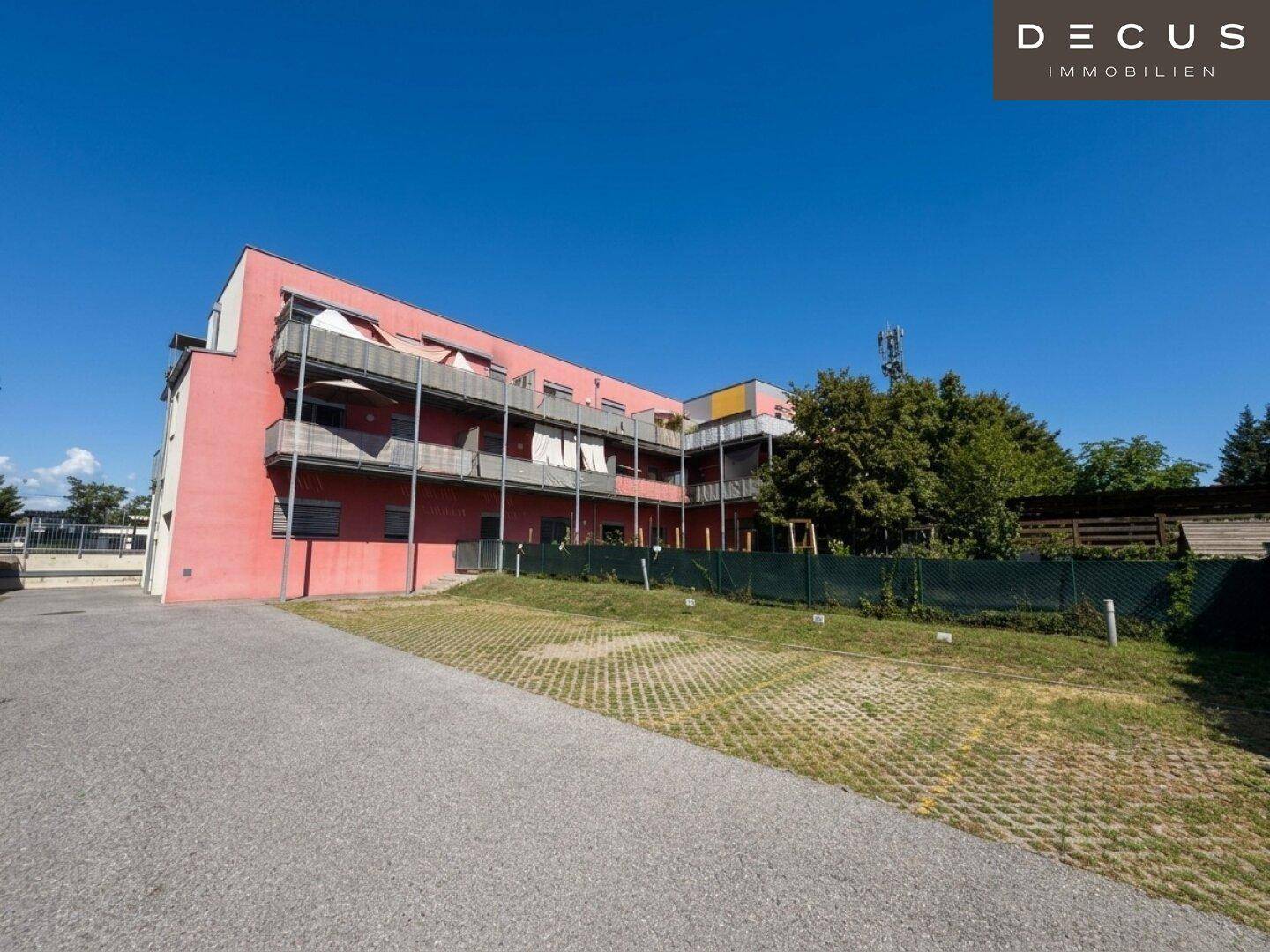 Weitläufige Außenansicht des modernen Wohngebäudes mit roter Fassade und Balkonen unter klarem Himmel.