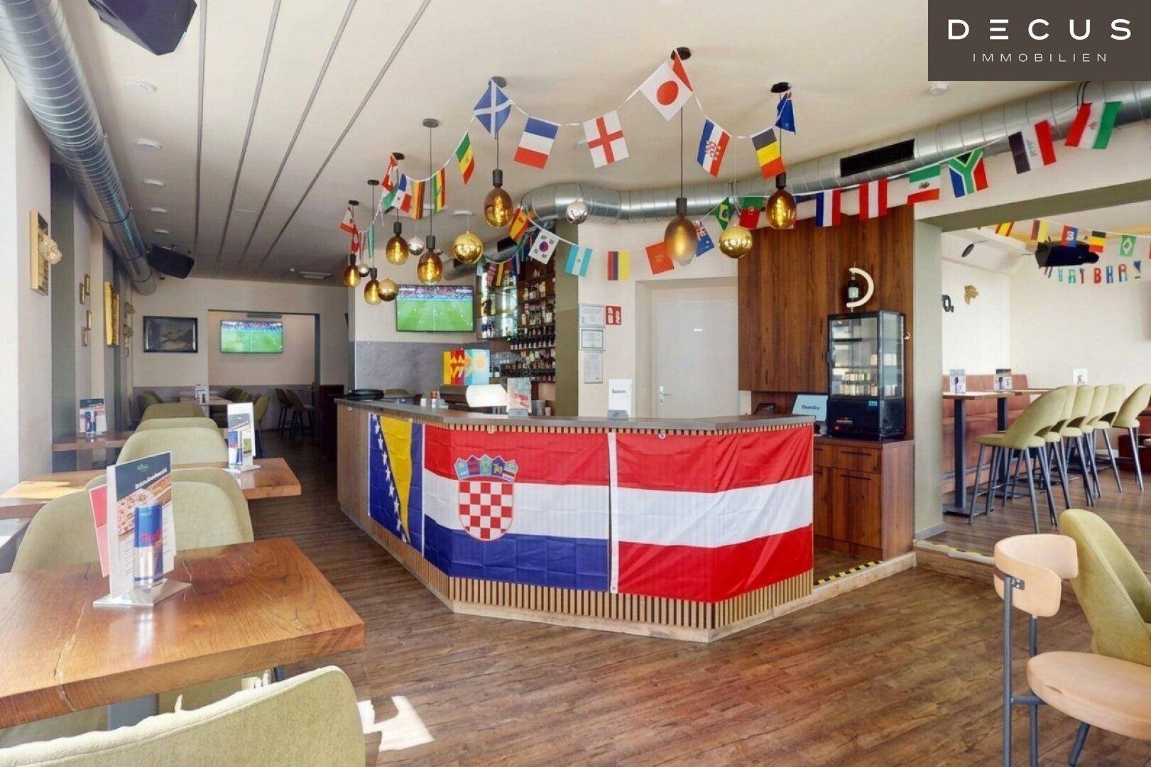 Hauptthekenbereich einer Bar oder eines Restaurants mit festlicher Flaggen-Dekoration und Bildschirmen.