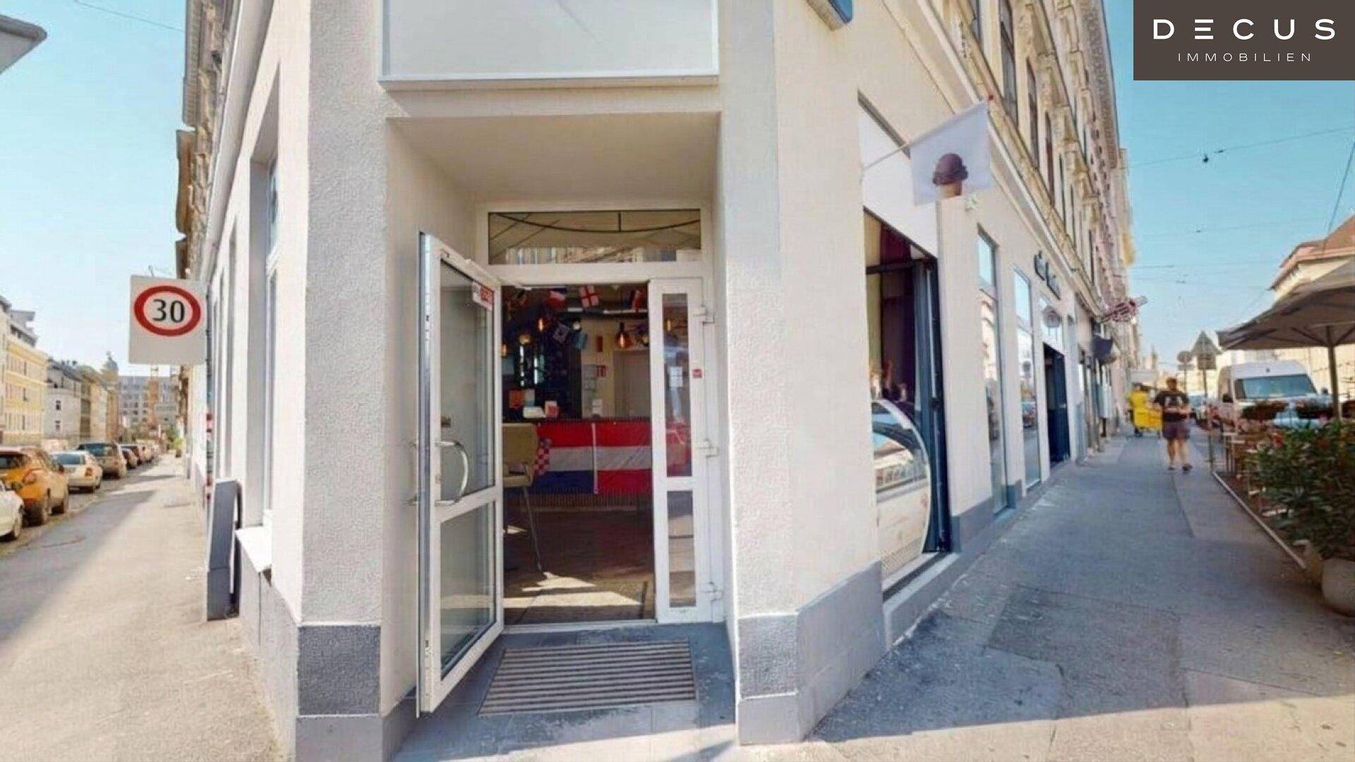 Eingangsbereich des Gebäudes an einer Straßenecke, mit geöffneter Tür und Blick in den Innenraum.