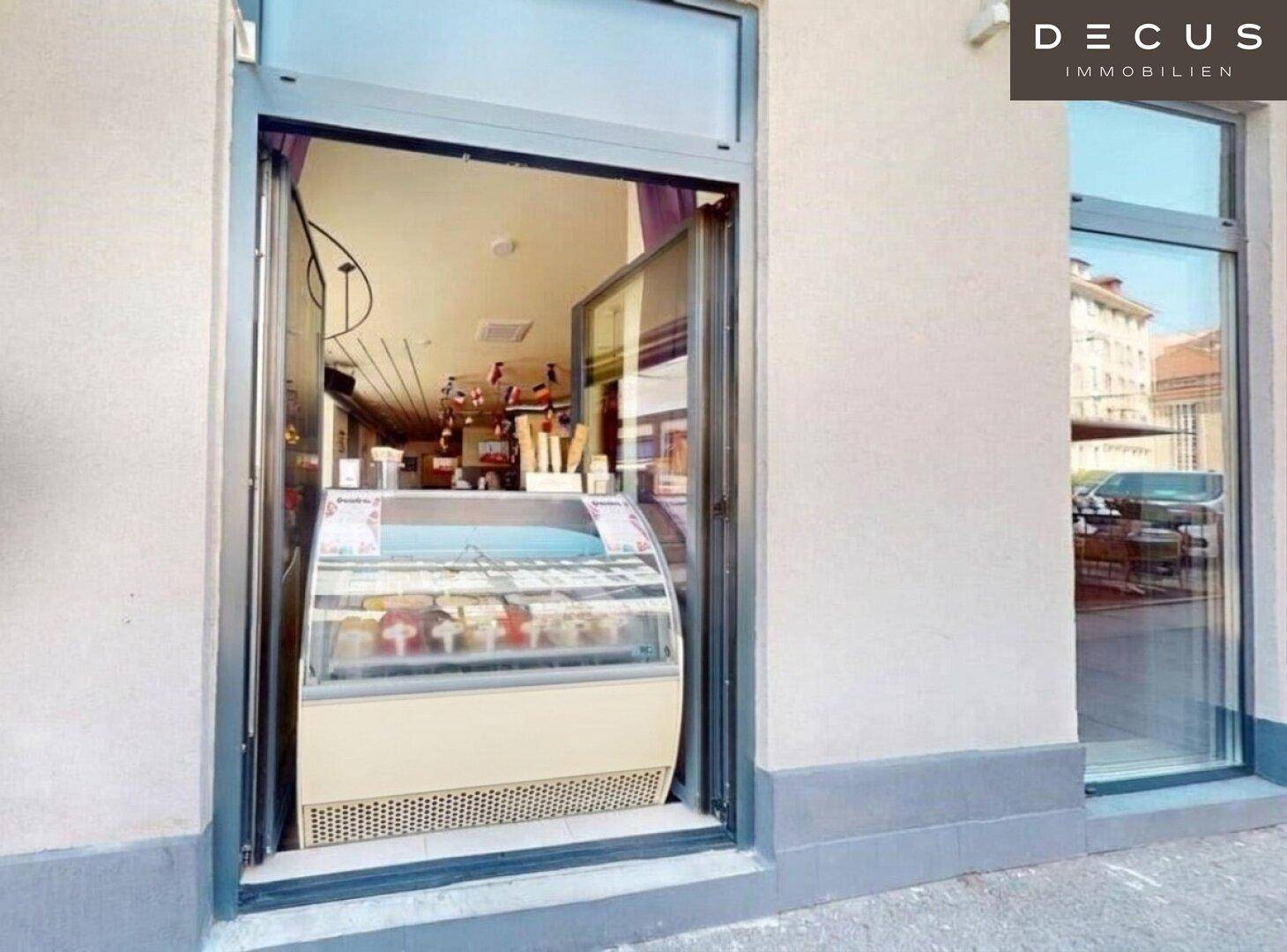 Schaufenster mit einer Eistruhe, die verschiedene Eissorten präsentiert, sichtbar von der Straße aus.