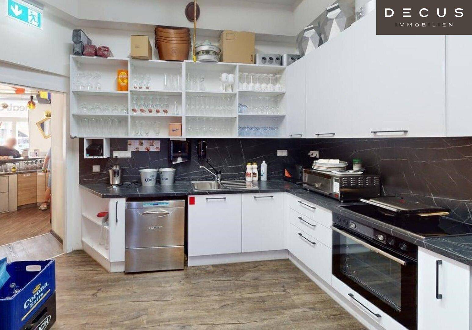 Funktionale Gewerbeküche mit weißen Schränken, dunklen Arbeitsplatten, Spülmaschine und Backofen für den Restaurantbetrieb.