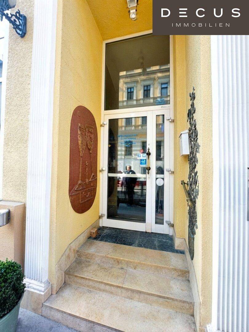 Eingangsbereich mit einer Glastür und Steinstufen, die zum Gebäude führen.