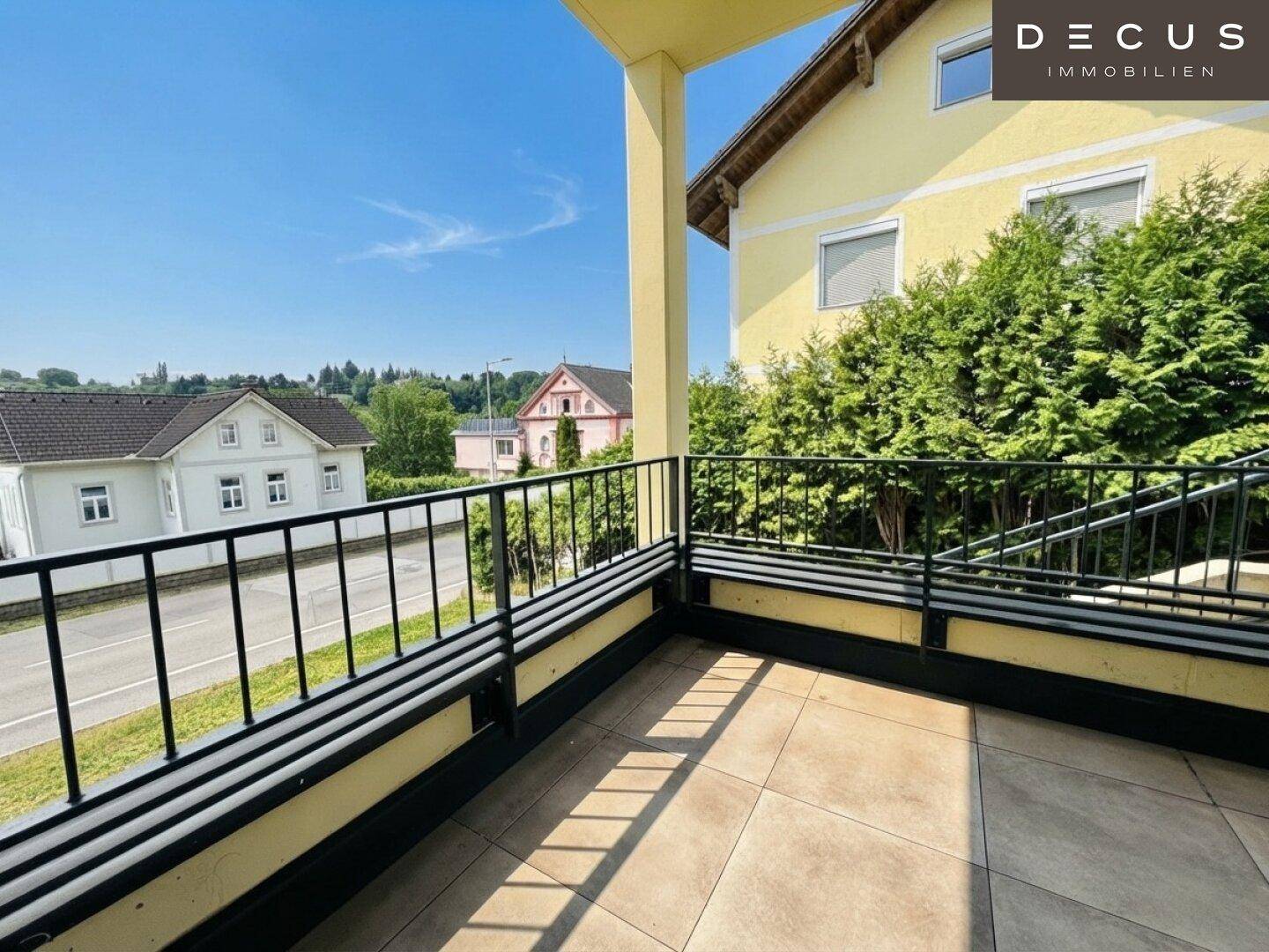 Sonniger Balkon mit Fliesenboden und Blick auf die Straße und umliegende Häuser.