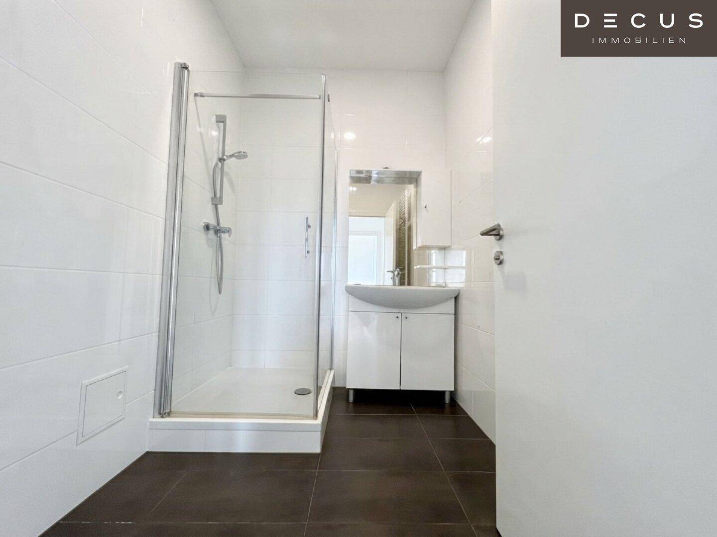 Modernes Badezimmer mit weiß gefliesten Wänden, dunklem Boden und einer Duschkabine.
